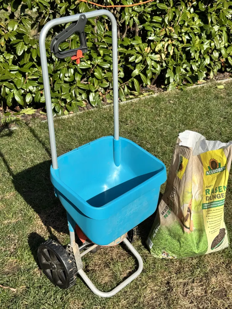 Gardena Schleuderstreuer XL befüllt mit organischem Neudorff Rasendünger auf dem Rasen.