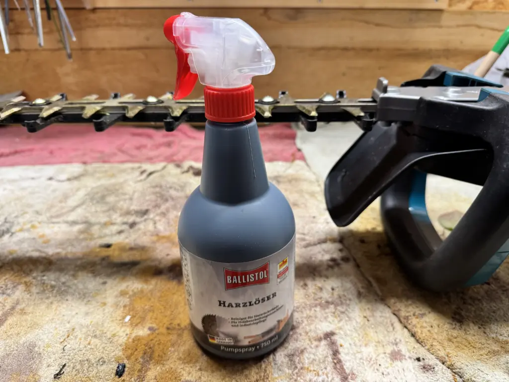 Die Ballistol Harzlöser Sprühflasche bereit zum Einsatz auf der Werkbank neben der verklebten Makita UH006G Heckenschere.