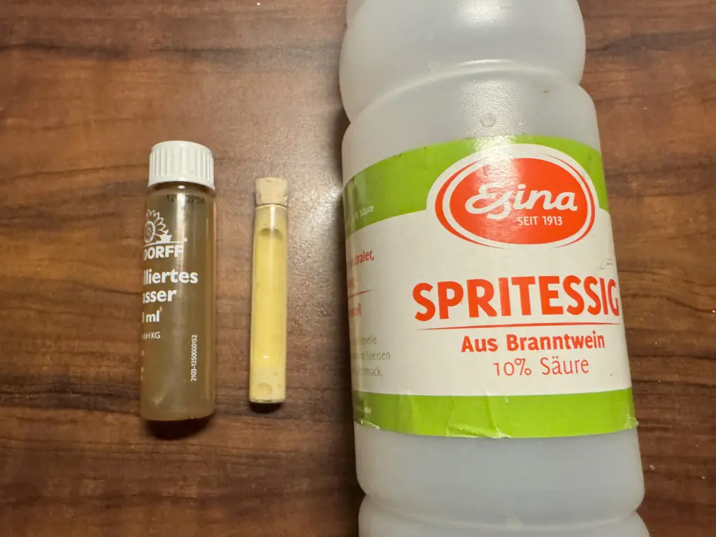 Neudorff pH-Bodentest im Säure-Stress-Test: Ein Röhrchen mit leuchtend gelber Flüssigkeit, daneben eine große Flasche Esina Spritessig mit 10% Säure auf Holzuntergrund.