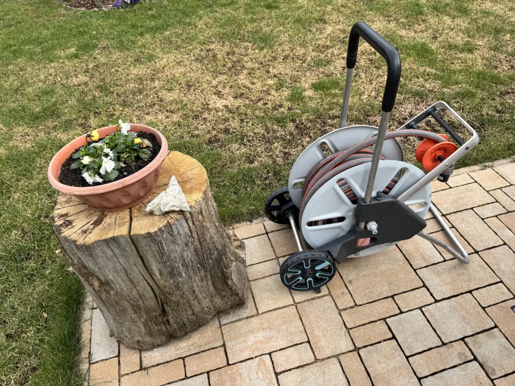 Der Gardena Schlauchwagen steht neben einem Baumstumpf auf einer gepflasterten Fläche.