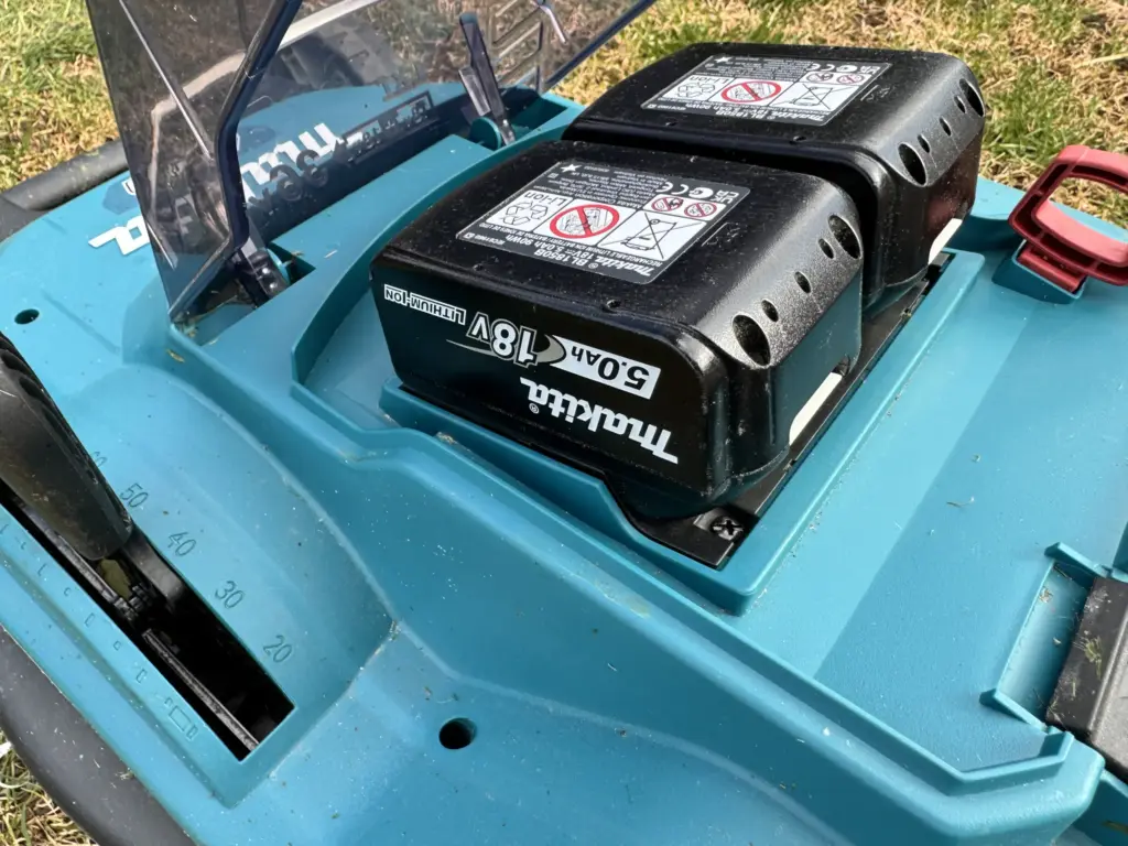 Im Paket DLM432PT2 sind zwei 5 Ah Akkus bereits enthalten, die den Akku-Rasenmäher genug Kraft geben - diese sind auf dem Foto in den Akku-Steckplätzen eingesteckt - die Kunststoffklappe ist geöffnet.