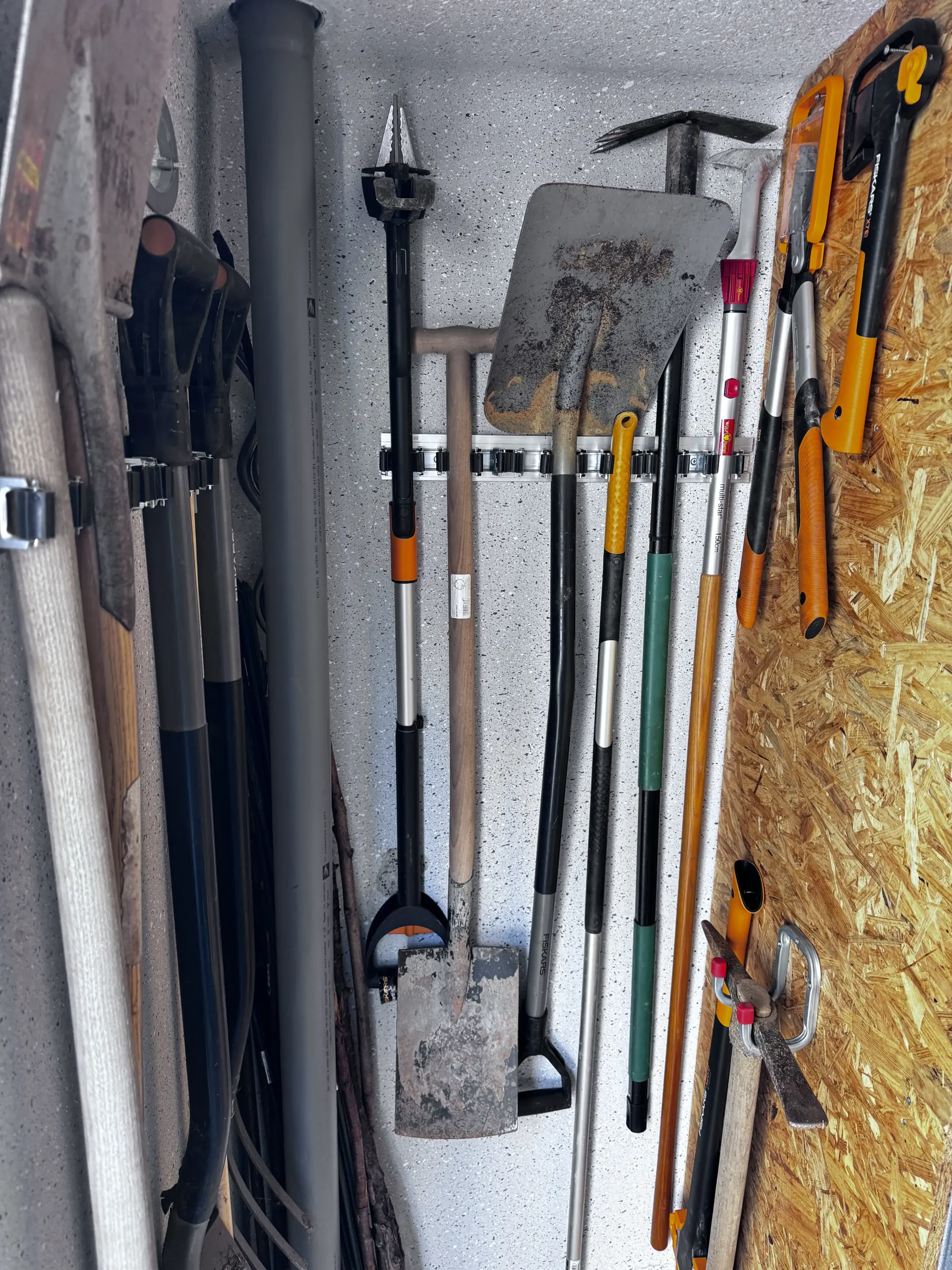 Fiskars Äxte, Spaltaxt und Astschere ordentlich sortiert an einer OSB-Wand im Geräteschuppen.