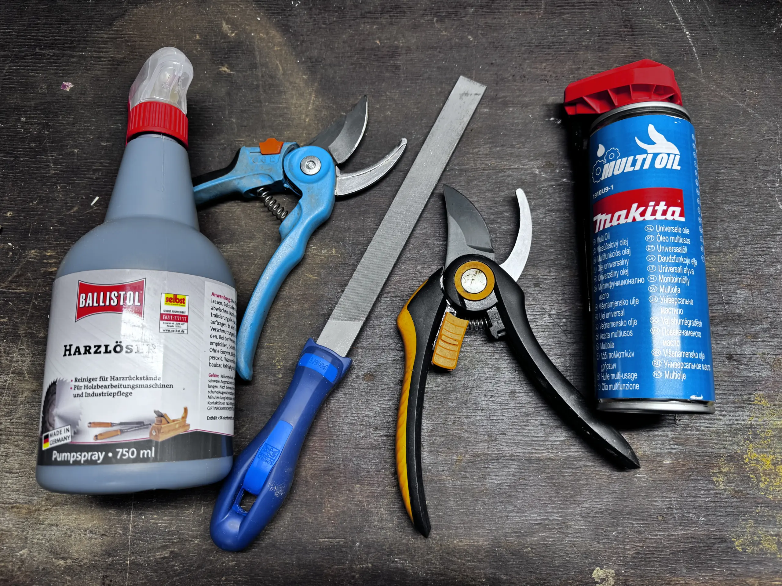 Auf einer Werkbank liegen zwei gereinigte und geschärfte Gartenscheren - daneben liegt eine Flasche Ballistol Harzlöser, eine Flachfeile und eine Dose Makita Multi-Öl.