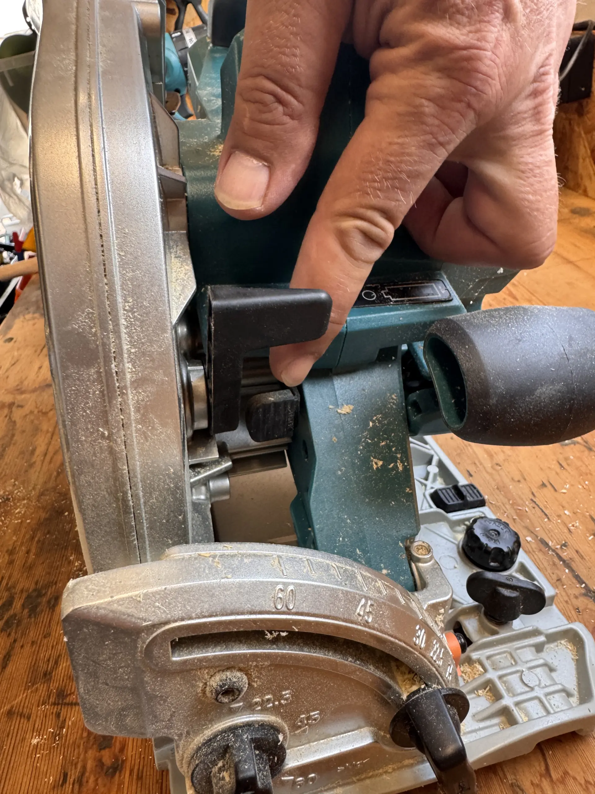 Finger zeigt auf die Spindelarretierung der Makita DHS900 beim Sägeblattwechsel