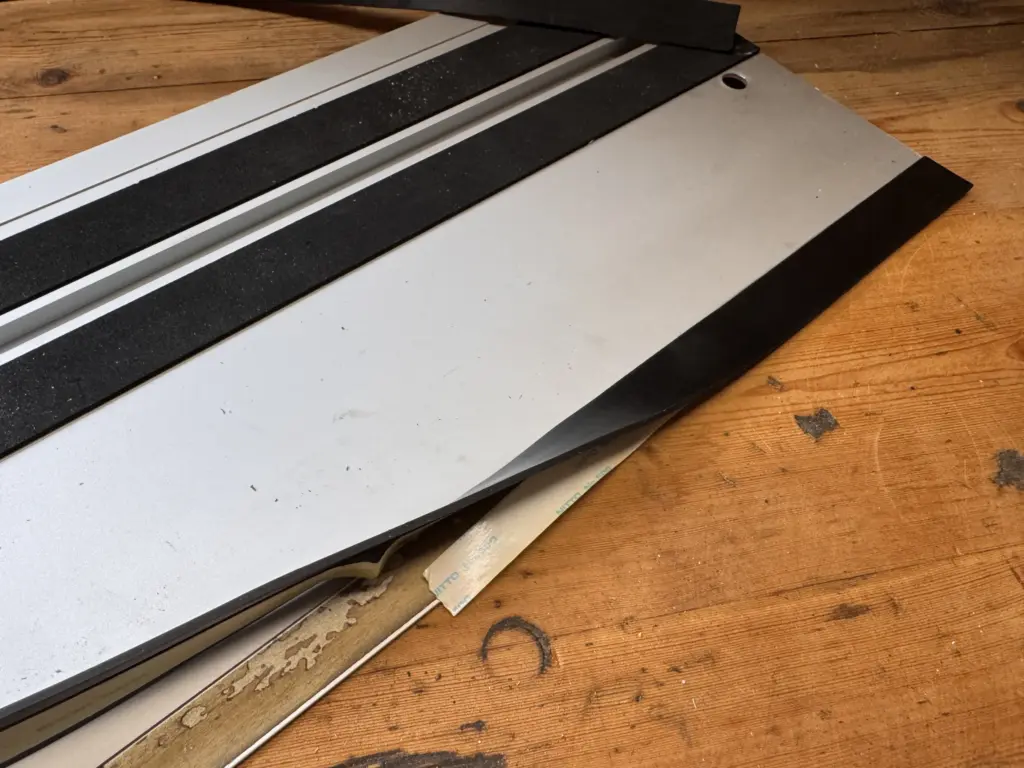Neuer Splitterschutz wird an der Anlagekante einer Makita Führungsschiene aufgeklebt