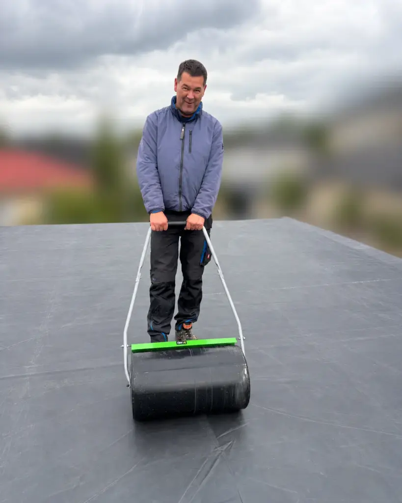 EPDM-Dachfolie auf dem Carport wird mit einer Rasenwalze angedrückt
