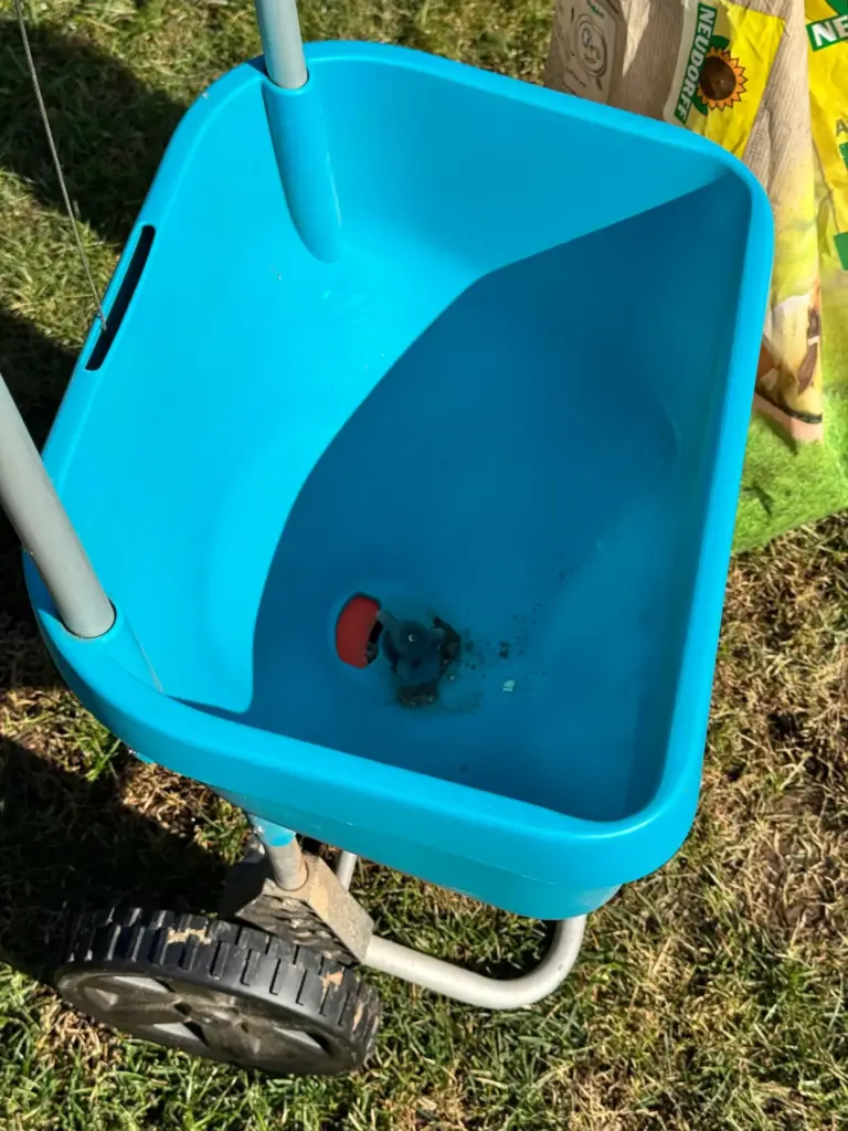 Leerer blauer Streugutbehälter meines Gardena XL Schleuderstreuers mit sichtbarer roter Auslassöffnung und Mechanik am Boden