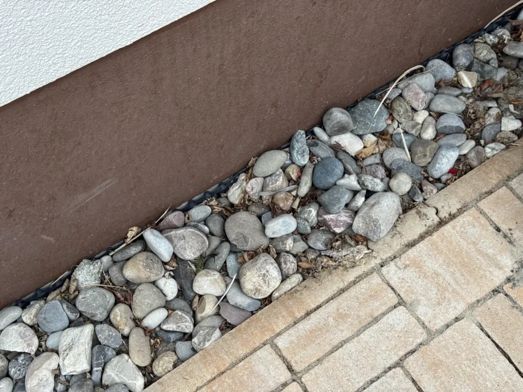 Laub auf Kies entfernen am Spritzschutz neben dem Haus
