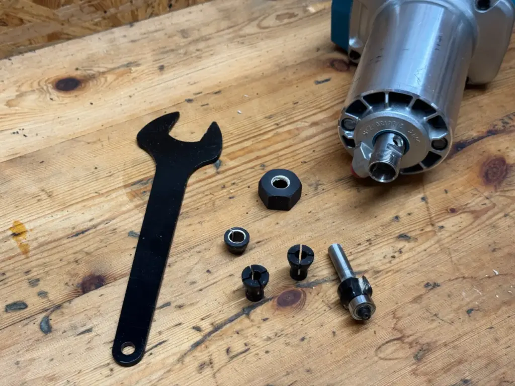 Makita DRT50 Zubehör: Zwei geschlitzte Spannzangen, Spannmutter, Schraubenschlüssel und Fräser neben der Motoreinheit
