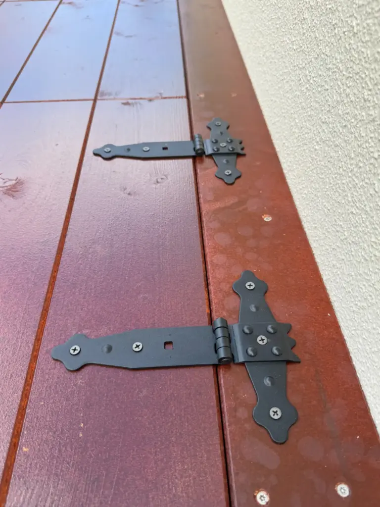 Schwarze Zier-Scharniere zur Befestigung der braunen Klappdeckel am Holzrahmen