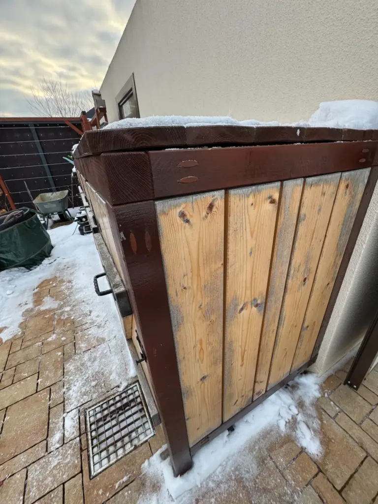 Seitenansicht der Mülltonnenbox im Schnee mit sichtbaren Holzverfärbungen