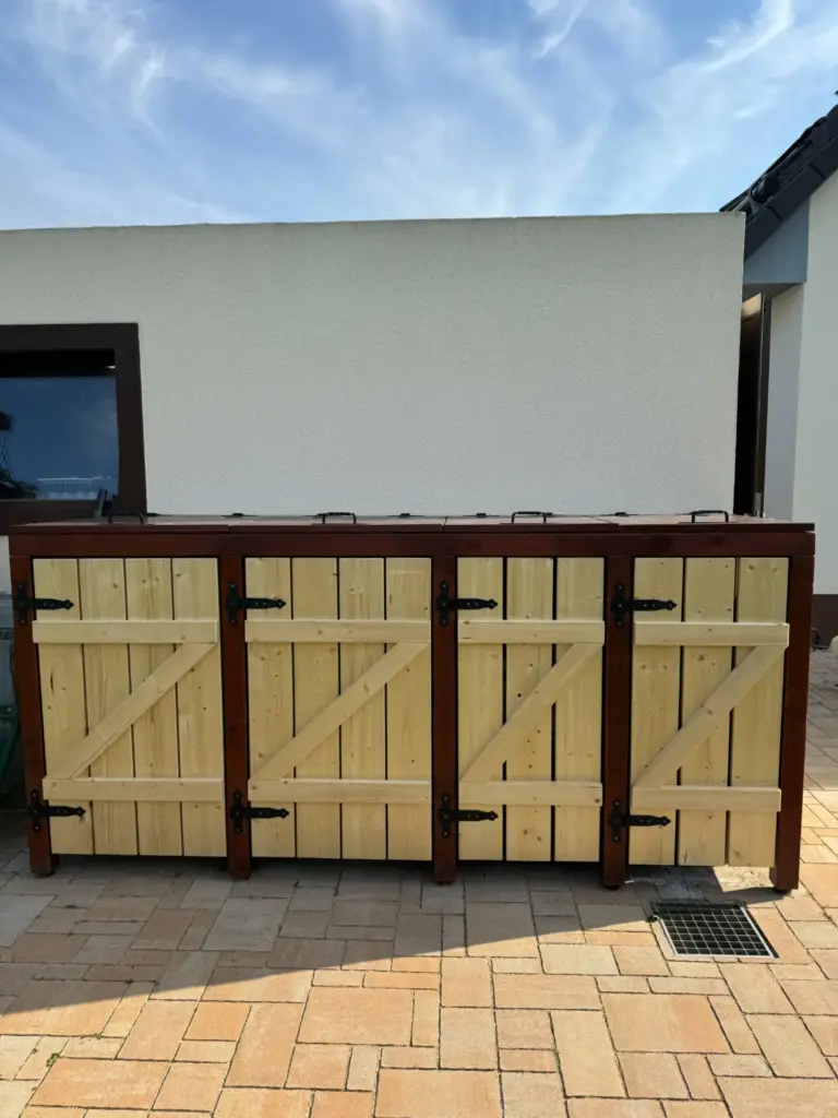 Mülltonnenbox aus Holz mit vier Türen und vier Klappdeckeln direkt neben der Garage