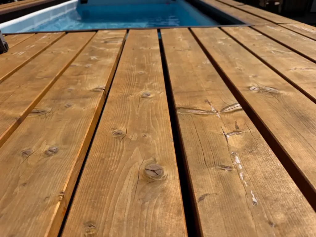 Waagerechte Bretter der Poolumrandung mit stellenweisen Aufhellungen und Gebrauchsspuren neben dem Schwimmbecken