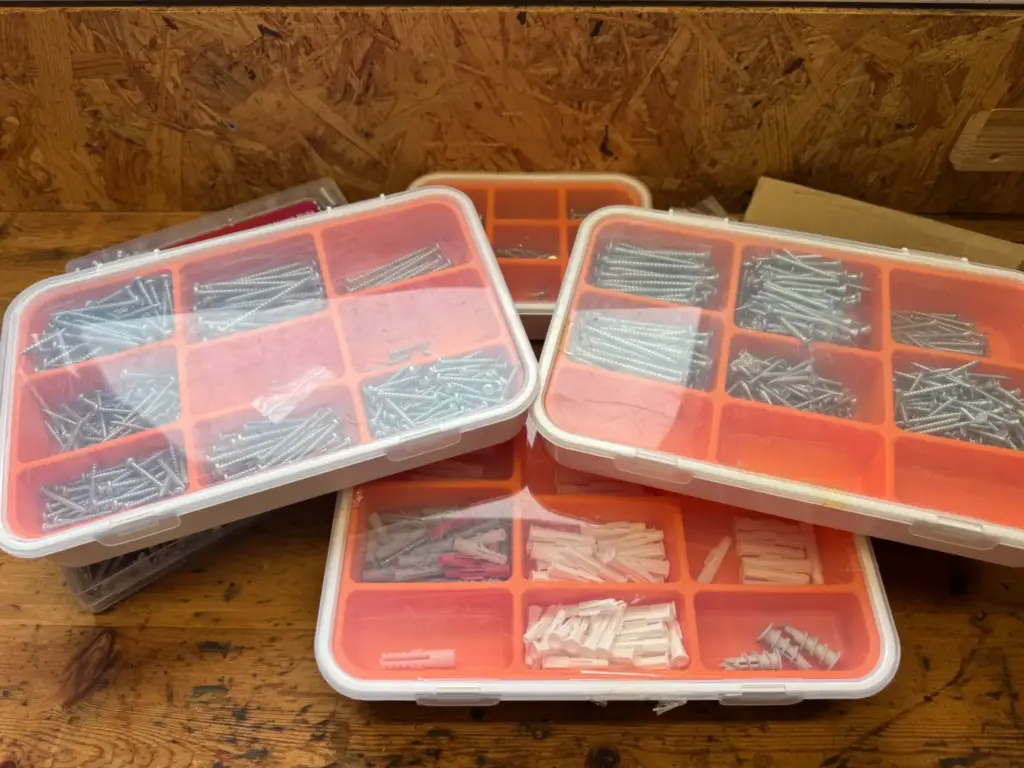 Mehrere transparente Sortimentskästen mit orangefarbenen Einsätzen, Schrauben und Dübeln.