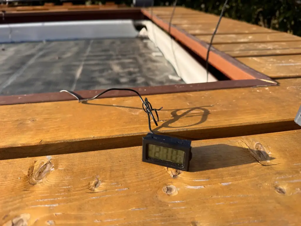 Digitales Thermometer mit Fühler am Holzrand des Aufstellpools zur Temperaturmessung
